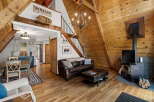 Experience rustic charm in this A-frame cabin living room, featuring a rich leather sofa, a striking chandelier, and a cozy wood-burning stove.