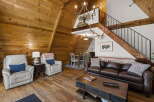 Experience rustic charm in this A-frame cabin living room, featuring warm wood paneling throughout and a cozy seating area with plush recliners and a leather sofa.