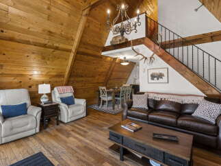Experience rustic charm in this A-frame cabin living room, featuring warm wood paneling throughout and a cozy seating area with plush recliners and a leather sofa.