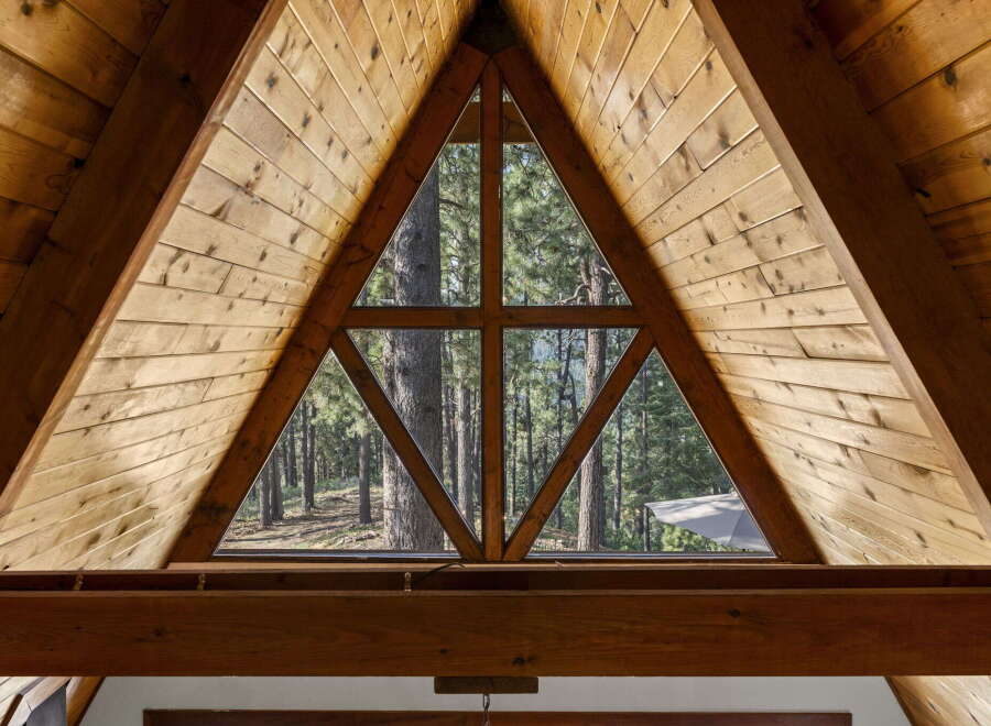 Experience the rustic charm of this A-frame cabin, featuring a unique triangular window that offers breathtaking views of the surrounding pine forest.