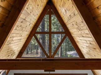 Experience the rustic charm of this A-frame cabin, featuring a unique triangular window that offers breathtaking views of the surrounding pine forest.
