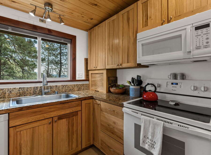 Experience rustic charm in this cozy cabin kitchen, featuring warm wood cabinetry and a stunning view through the large window.