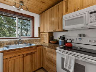 Experience rustic charm in this cozy cabin kitchen, featuring warm wood cabinetry and a stunning view through the large window.