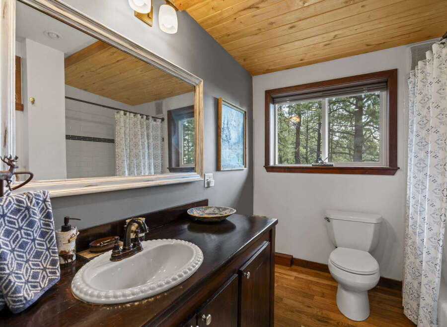 This charming bathroom features a rustic wooden ceiling and a large vanity with a white basin sink.
