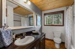 This charming bathroom features a rustic wooden ceiling and a large vanity with a white basin sink.