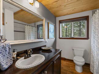 This charming bathroom features a rustic wooden ceiling and a large vanity with a white basin sink.