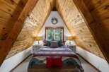 Experience rustic charm in this A-frame bedroom, featuring a cozy bed adorned with a vibrant, geometric-patterned comforter and plush pillows.