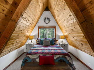 Experience rustic charm in this A-frame bedroom, featuring a cozy bed adorned with a vibrant, geometric-patterned comforter and plush pillows.