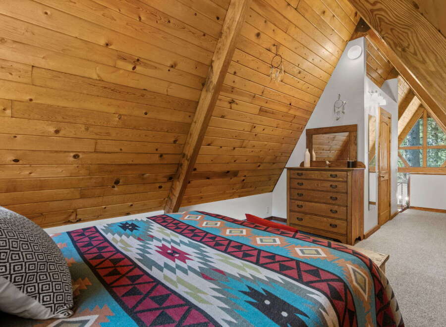 Experience rustic charm in this A-frame bedroom, featuring a cozy bed adorned with a vibrant Native American-inspired blanket.