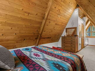 Experience rustic charm in this A-frame bedroom, featuring a cozy bed adorned with a vibrant Native American-inspired blanket.
