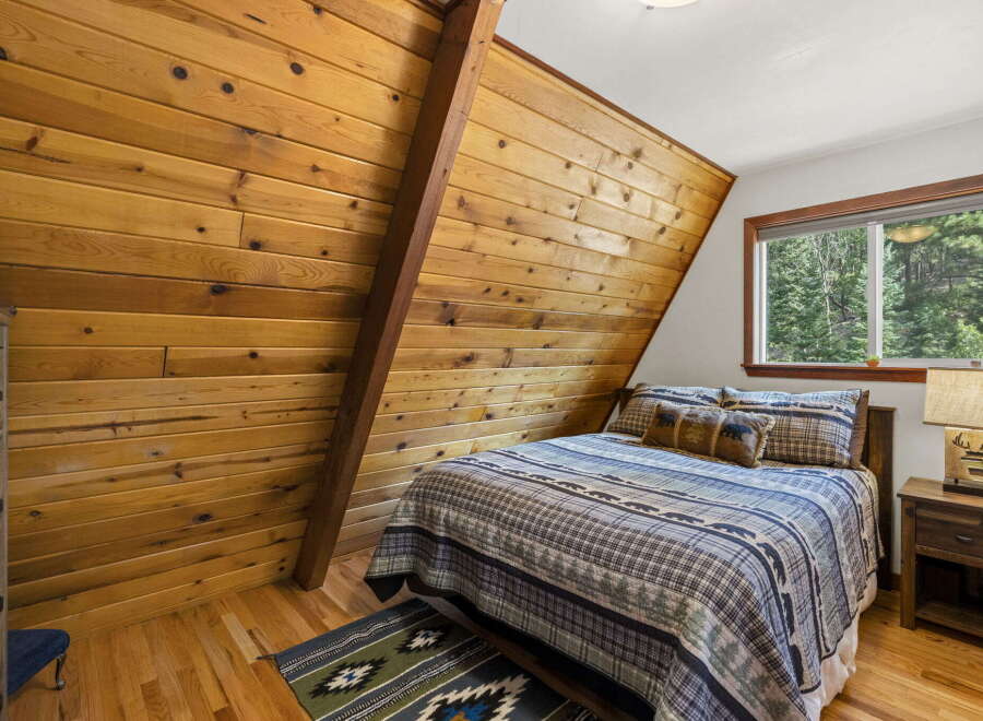 Cozy A-frame bedroom featuring warm wood paneling and a comfortable queen-size bed adorned with rustic bedding.