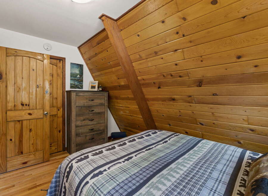 Experience rustic charm in this cozy bedroom featuring a wooden plank accent wall and a comfortable bed with a nature-themed comforter.