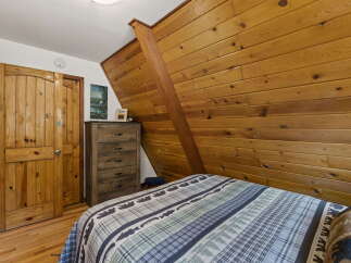 Experience rustic charm in this cozy bedroom featuring a wooden plank accent wall and a comfortable bed with a nature-themed comforter.