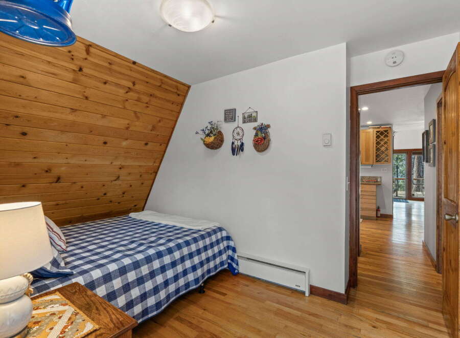 Discover cozy living in this charming bedroom featuring a unique wood-paneled A-frame wall and a classic blue and white checkered bedspread.