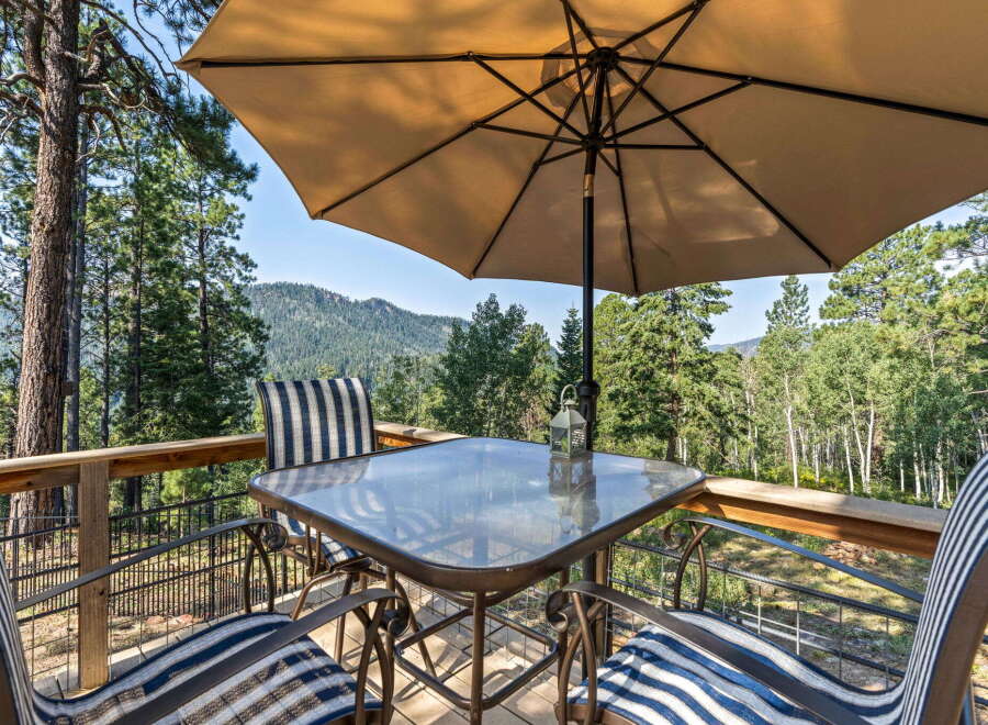 Enjoy breathtaking mountain views from this charming deck, complete with a glass-top table and comfortable seating under a large umbrella.