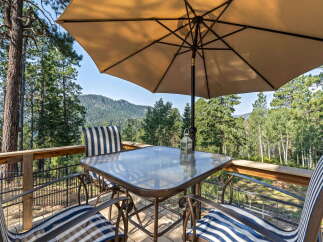 Enjoy breathtaking mountain views from this charming deck, complete with a glass-top table and comfortable seating under a large umbrella.