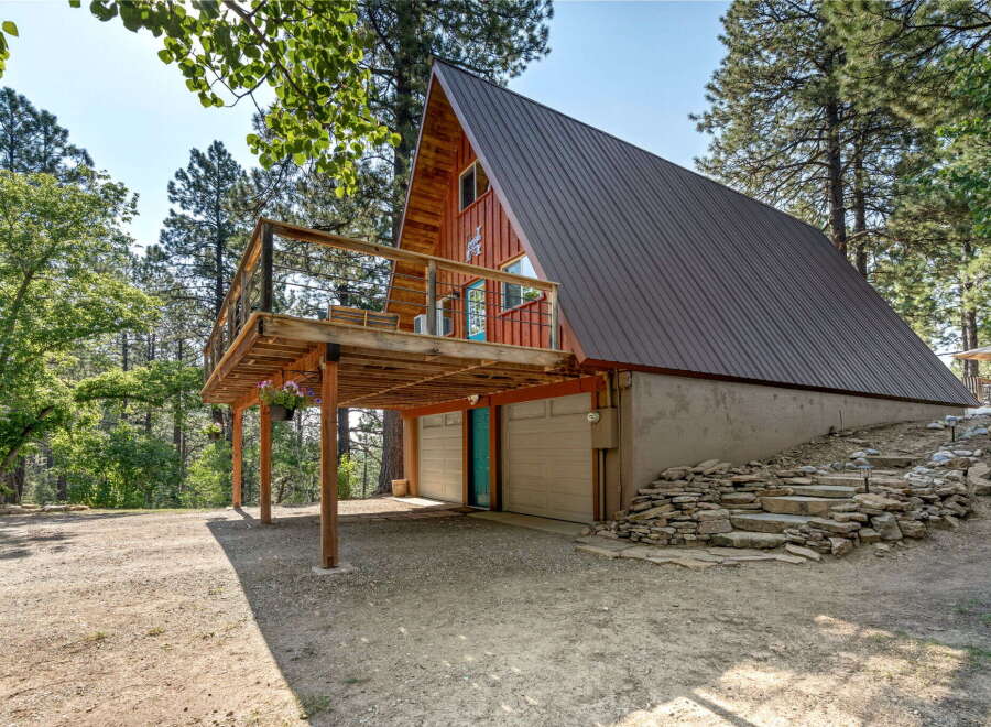 Discover this unique A-frame cabin nestled amongst tall pine trees, featuring a spacious wooden deck perfect for enjoying the serene surroundings.