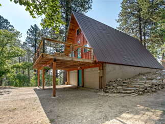 Discover this unique A-frame cabin nestled amongst tall pine trees, featuring a spacious wooden deck perfect for enjoying the serene surroundings.