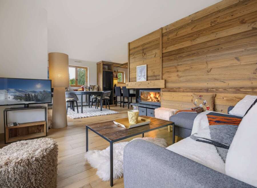 Experience cozy mountain living in this charming living room, featuring a stunning wood-paneled wall and a crackling fireplace.