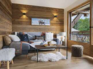 Experience cozy mountain living in this charming living room featuring rustic wood-paneled walls and a comfortable sofa adorned with decorative pillows and throws.