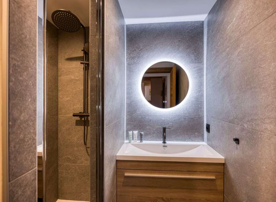 Experience modern luxury in this beautifully appointed bathroom, featuring a sleek walk-in shower with a rainfall showerhead and a stylish vanity with a backlit circular mirror.