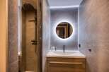 Experience modern luxury in this beautifully appointed bathroom, featuring a sleek walk-in shower with a rainfall showerhead and a stylish vanity with a backlit circular mirror.