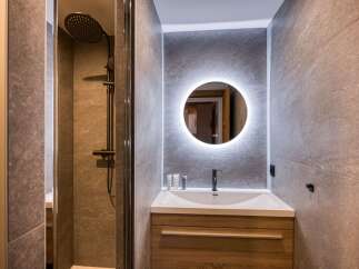 Experience modern luxury in this beautifully appointed bathroom, featuring a sleek walk-in shower with a rainfall showerhead and a stylish vanity with a backlit circular mirror.