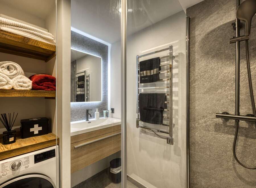 This modern bathroom features a sleek vanity with a vessel sink and a wooden cabinet, complemented by a large, illuminated mirror.