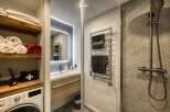 This modern bathroom features a sleek vanity with a vessel sink and a wooden cabinet, complemented by a large, illuminated mirror.