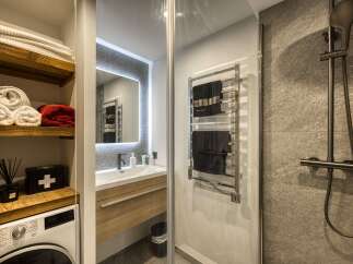 This modern bathroom features a sleek vanity with a vessel sink and a wooden cabinet, complemented by a large, illuminated mirror.