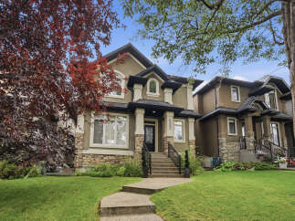 This stunning two-story home boasts a charming stone and stucco exterior, complemented by lush green landscaping and mature trees.