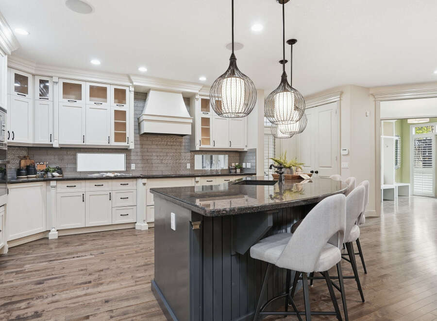 Experience luxury in this stunning kitchen featuring elegant white cabinetry, a spacious granite island with bar seating, and a modern vent hood.