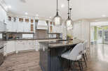 Experience luxury in this stunning kitchen featuring elegant white cabinetry, a spacious granite island with bar seating, and a modern vent hood.