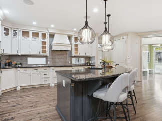 Experience luxury in this stunning kitchen featuring elegant white cabinetry, a spacious granite island with bar seating, and a modern vent hood.