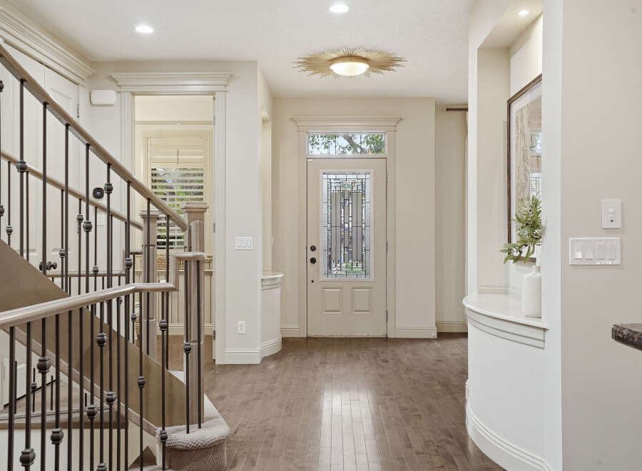 Step into this elegant entryway featuring a grand staircase with a wrought-iron railing and a beautiful stained-glass front door.