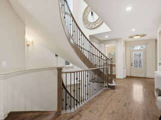 Step into a grand foyer featuring a stunning curved staircase with ornate railings and a decorative mirror accent.