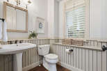 This charming bathroom features a classic pedestal sink with elegant bronze fixtures, complemented by a white beadboard wainscoting and dark wood flooring.