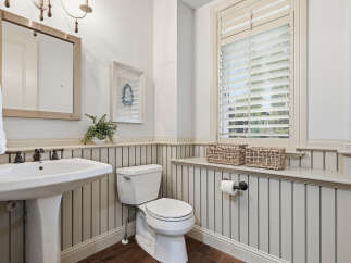 This charming bathroom features a classic pedestal sink with elegant bronze fixtures, complemented by a white beadboard wainscoting and dark wood flooring.
