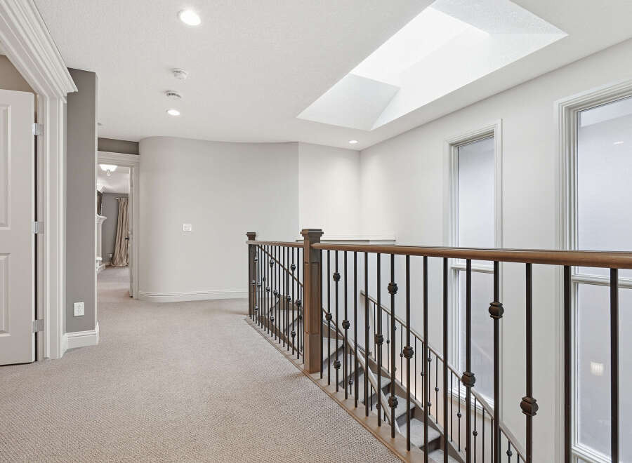 This spacious hallway features a beautiful wooden banister leading down a carpeted staircase.