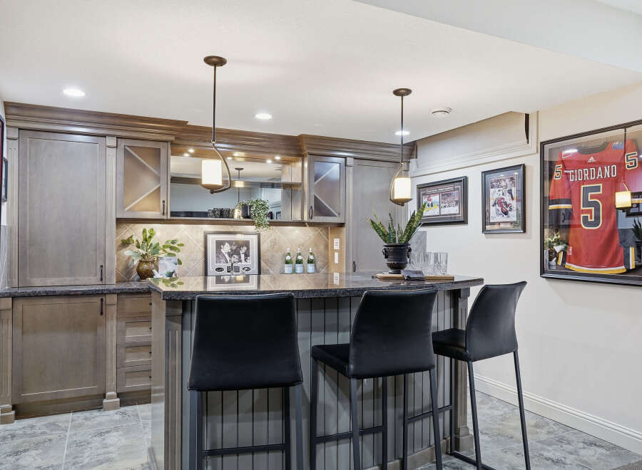 This stunning basement bar features custom grey cabinetry with glass-fronted upper cabinets and a granite countertop.