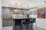 This stunning basement bar features custom grey cabinetry with glass-fronted upper cabinets and a granite countertop.