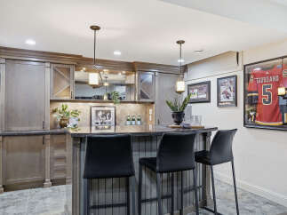 This stunning basement bar features custom grey cabinetry with glass-fronted upper cabinets and a granite countertop.