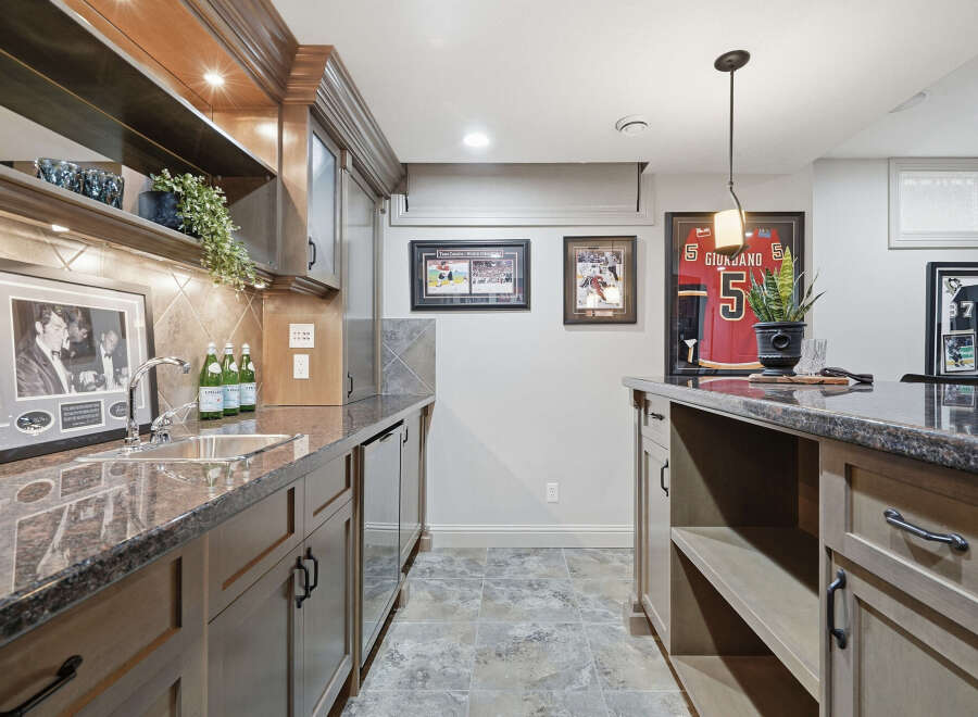 This basement bar area features a granite countertop with a stainless steel sink and faucet, complemented by custom wood cabinetry.