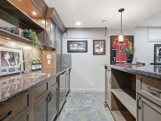 This basement bar area features a granite countertop with a stainless steel sink and faucet, complemented by custom wood cabinetry.