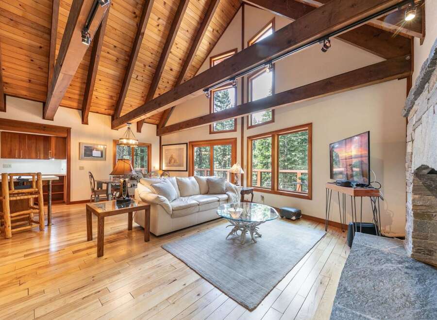 Experience rustic charm in this spacious living area featuring a vaulted wood-beamed ceiling and a grand stone fireplace.
