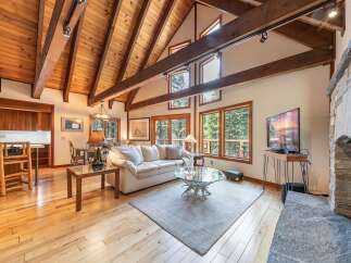 Experience rustic charm in this spacious living area featuring a vaulted wood-beamed ceiling and a grand stone fireplace.