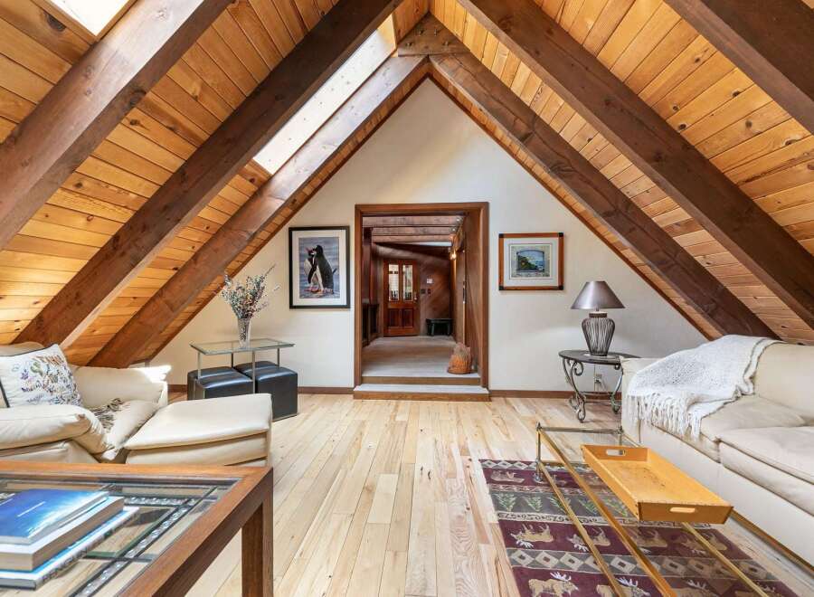 Experience rustic charm in this attic living space, featuring exposed wooden beams and a vaulted ceiling with skylights that flood the room with natural light.