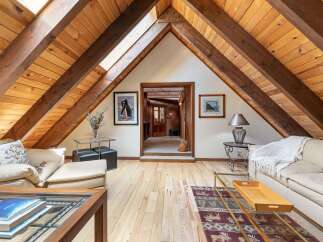 Experience rustic charm in this attic living space, featuring exposed wooden beams and a vaulted ceiling with skylights that flood the room with natural light.