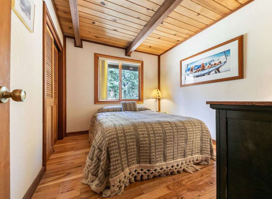Experience cozy cabin living in this charming bedroom featuring a comfortable bed adorned with a textured throw and decorative pillows.