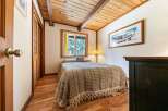 Experience cozy cabin living in this charming bedroom featuring a comfortable bed adorned with a textured throw and decorative pillows.